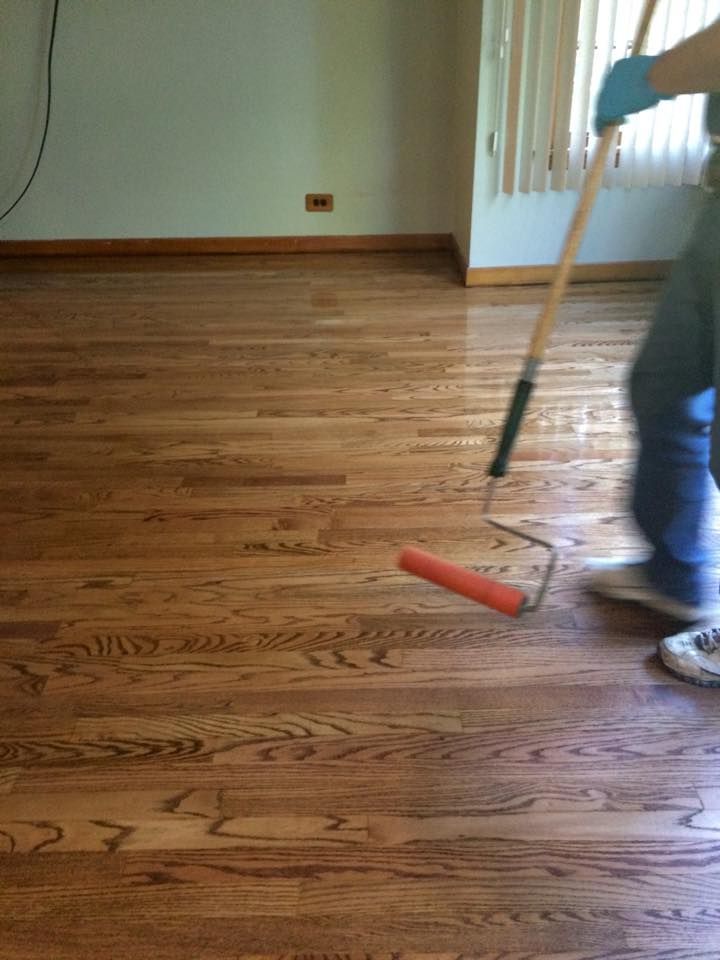 A person is painting a wooden floor with a roller.