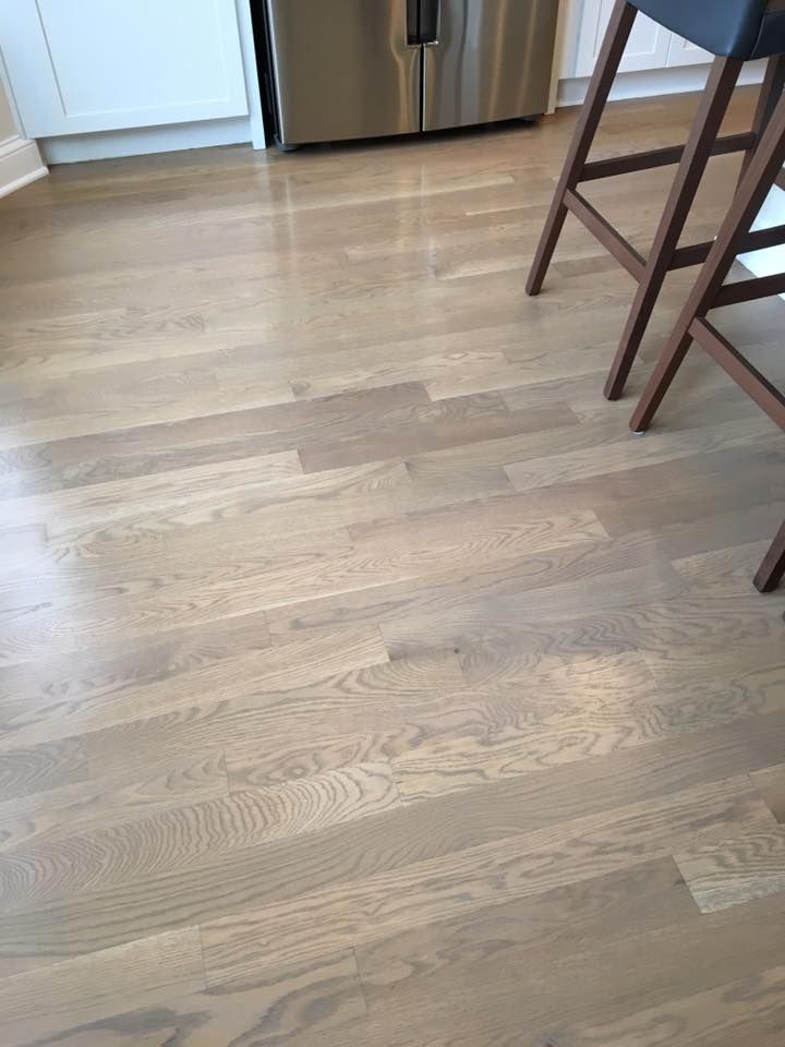 A kitchen with hardwood floors and stools and a refrigerator.