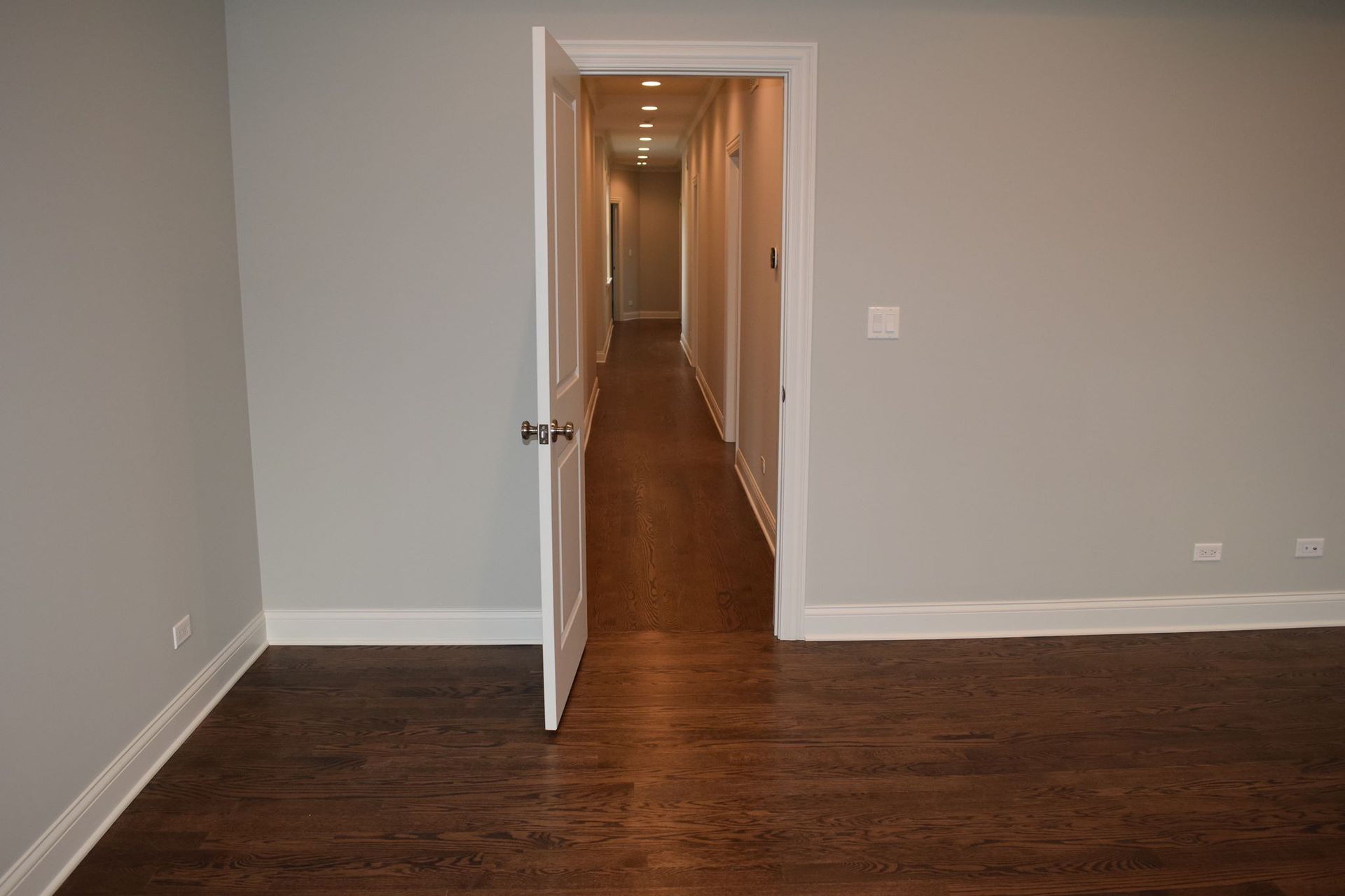 An empty room with hardwood floors and a long hallway leading to another room.