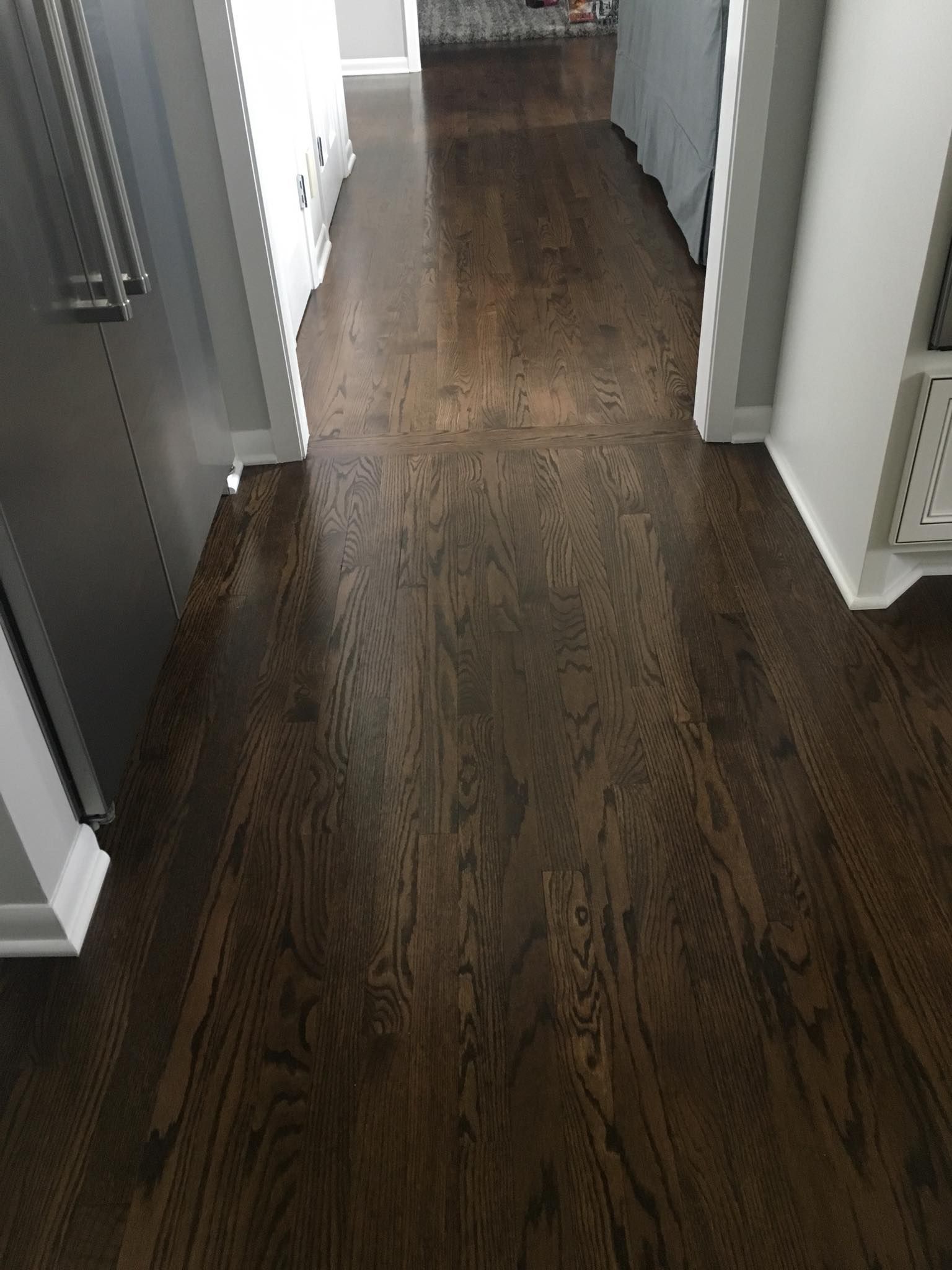 A dark wooden floor in a hallway leading to a kitchen.