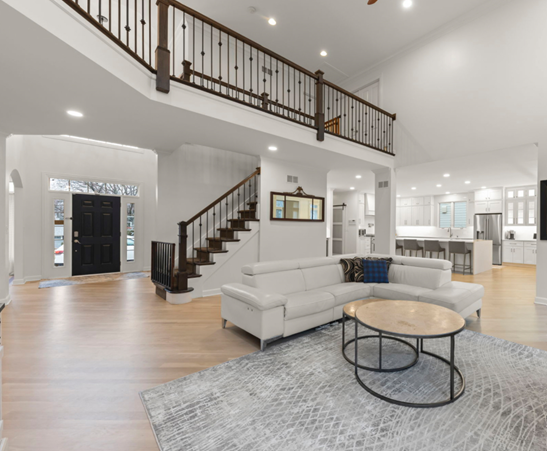 Spacious living room with a white sectional, rug, and stairs leading to an upper level with a railing.