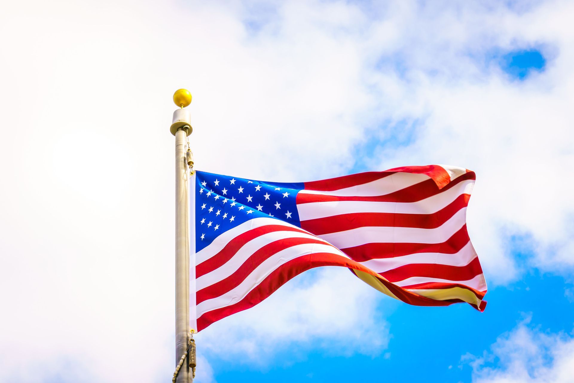 American flag waving on a flagpole against a blue sky with clouds