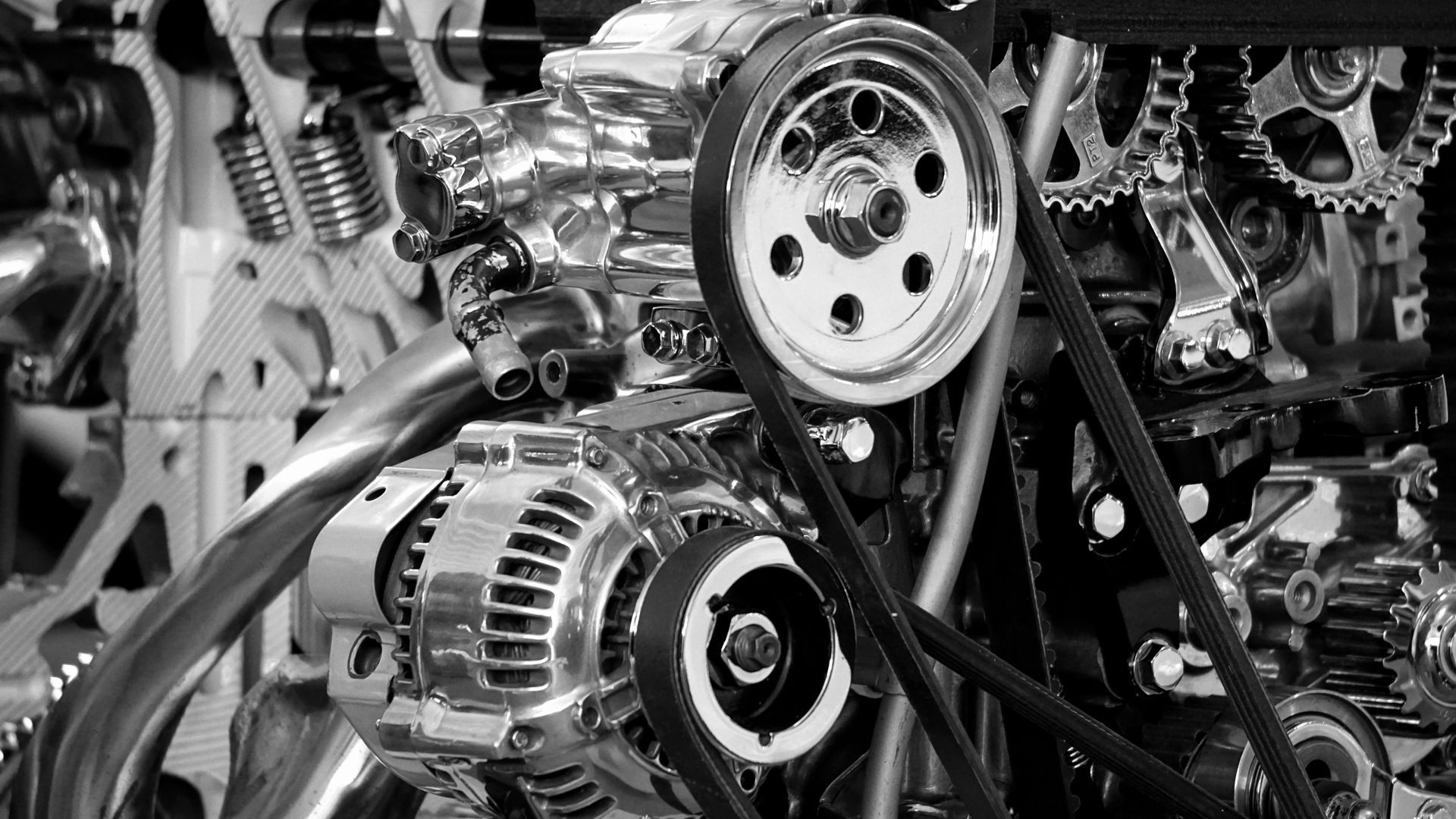 Close-up of a car engine with belts, pulleys, and metal components in black and white