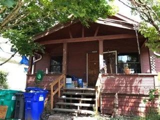 A red house with a porch and blue trash cans in front of it
