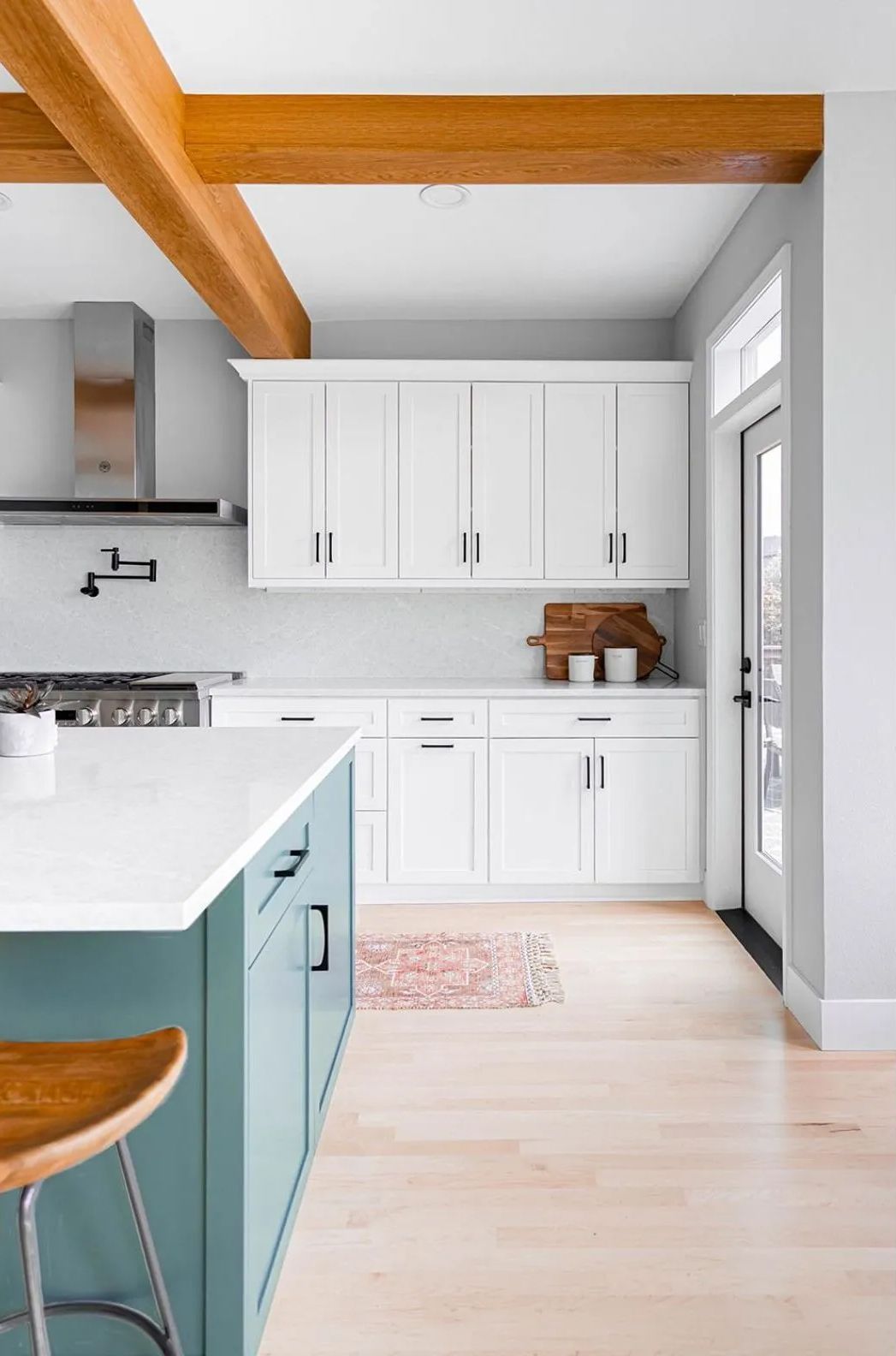 A kitchen with white cabinets and green cabinets and wooden beams.