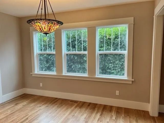 An empty room with three windows and a chandelier hanging from the ceiling.