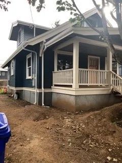 A blue house with a white porch is sitting on top of a dirt hill.