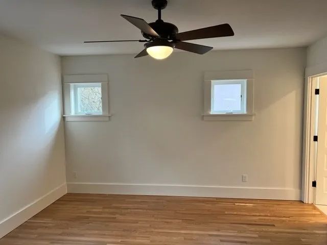 An empty room with a ceiling fan and two windows