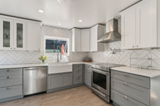 Modern kitchen with white and gray cabinets, stainless steel appliances, and a white herringbone backsplash.