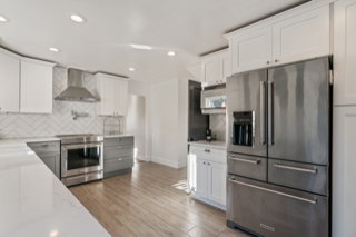 Modern kitchen with white and gray cabinets, stainless steel appliances, and light wood floors.