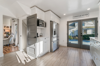 Bright, airy kitchen with white cabinets, stainless steel appliances, and gray accents, including a door leading to a living room and a doorway to the outside.