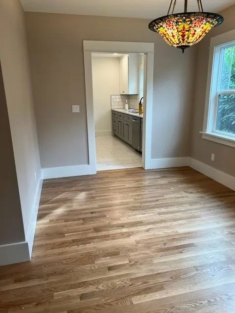 An empty room with hardwood floors and a chandelier hanging from the ceiling.
