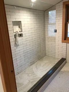 A bathroom with white brick walls and a walk in shower with a glass door.