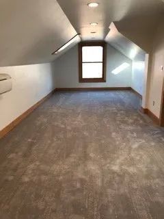 An empty attic with a window and a carpeted floor.