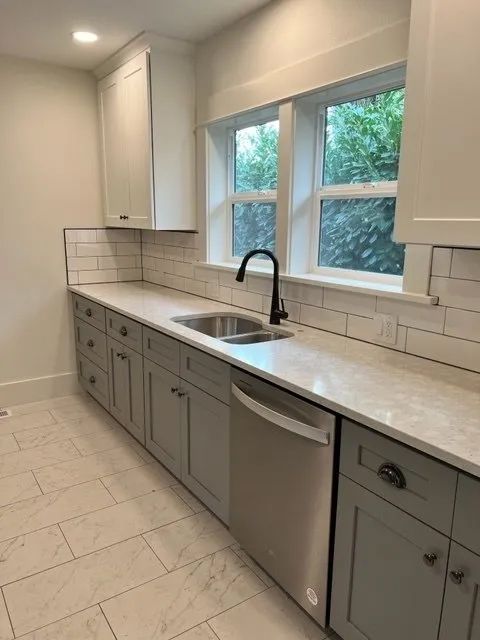 A kitchen with a sink, dishwasher, and two windows.