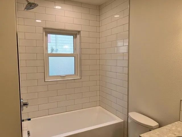 A bathroom with a bathtub, toilet, shower and window.