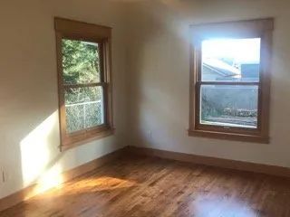 An empty room with hardwood floors and two windows.