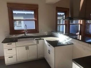 A kitchen with white cabinets, black counter tops, a sink and a window.