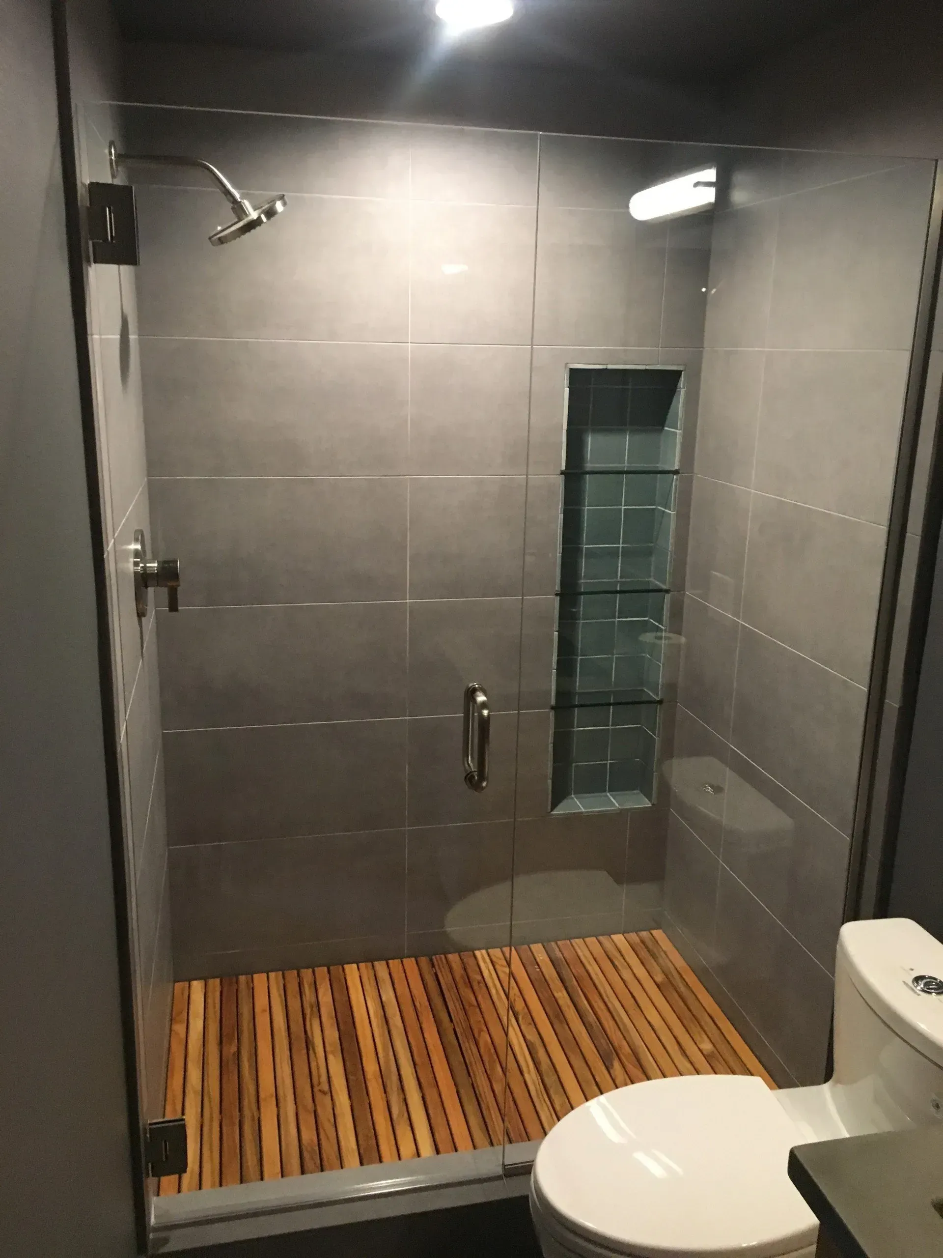 A bathroom with a toilet and a shower with a wooden floor.