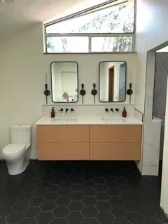 A bathroom with two sinks , a toilet , and two mirrors.