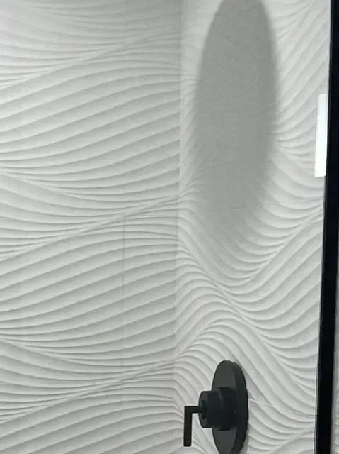 A shower stall with a black shower head and a white wall.