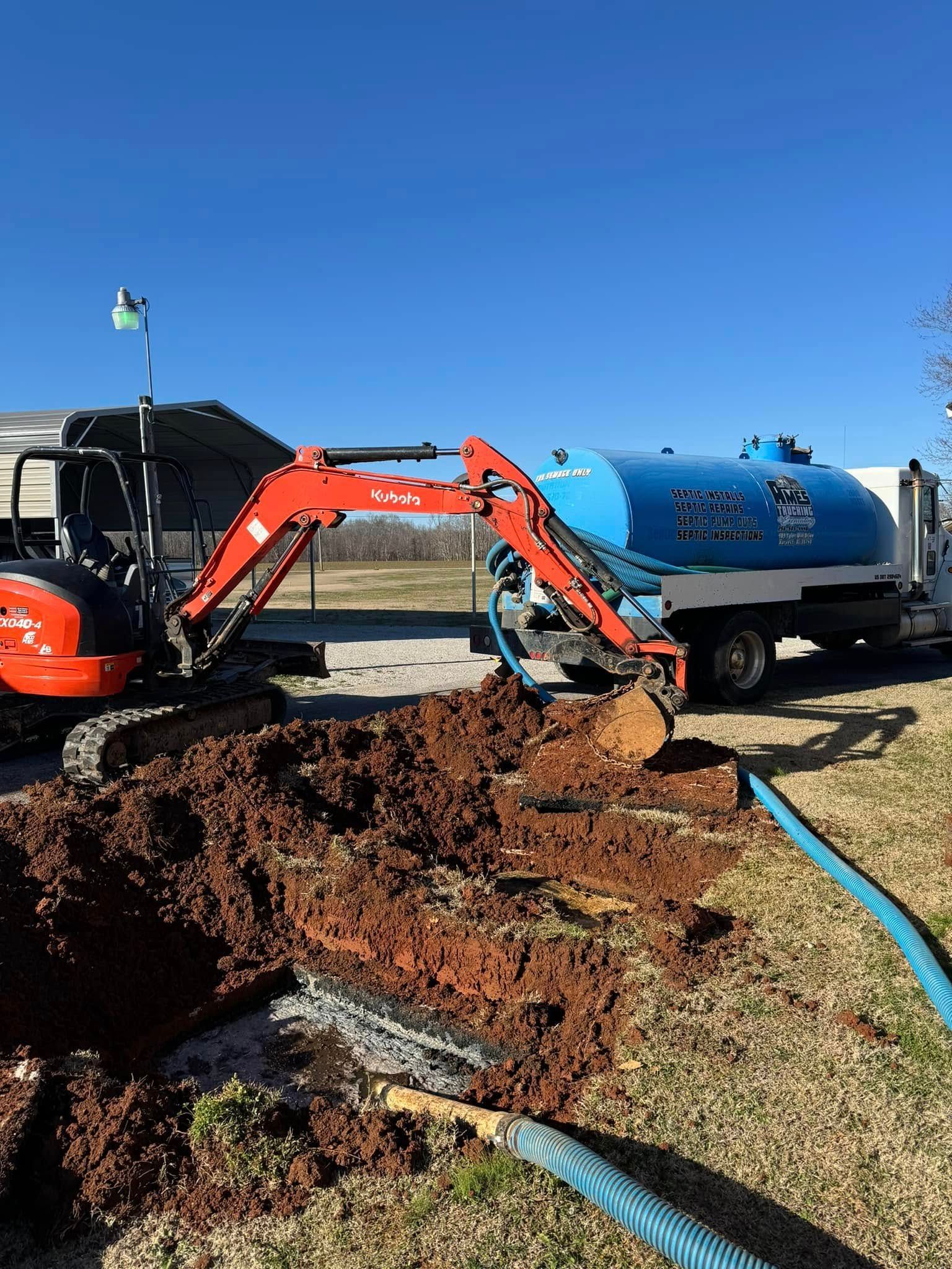 An excavator is digging a hole in the ground next to a septic tank.