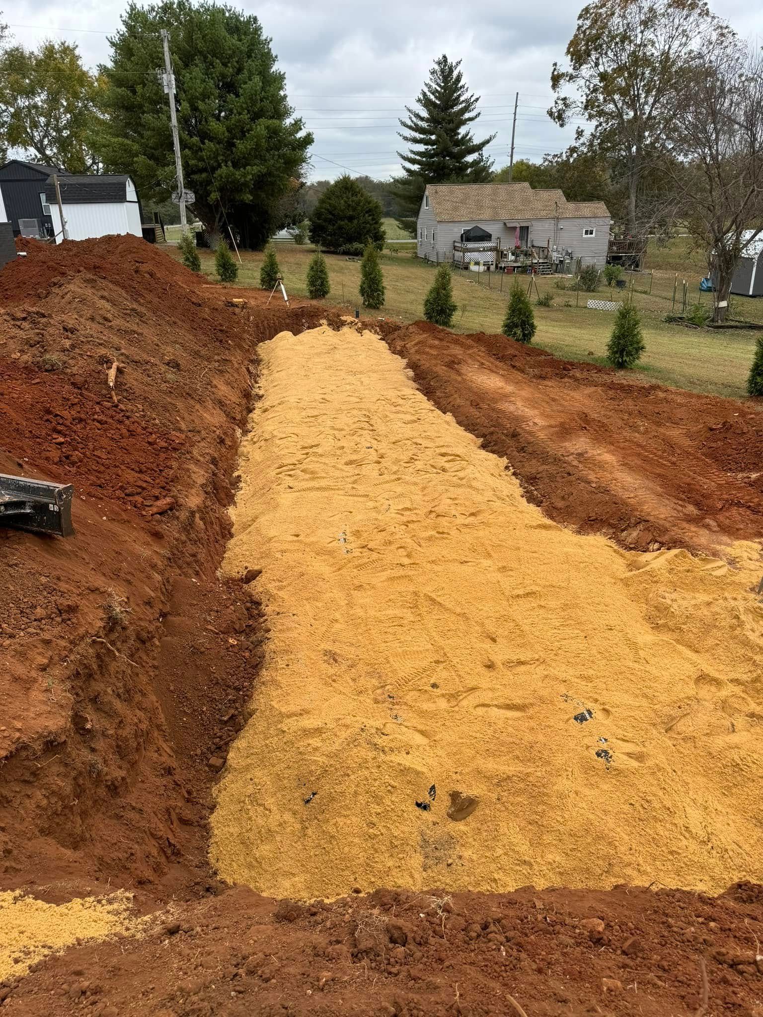 A dirt road is being built in a field with a house in the background.
