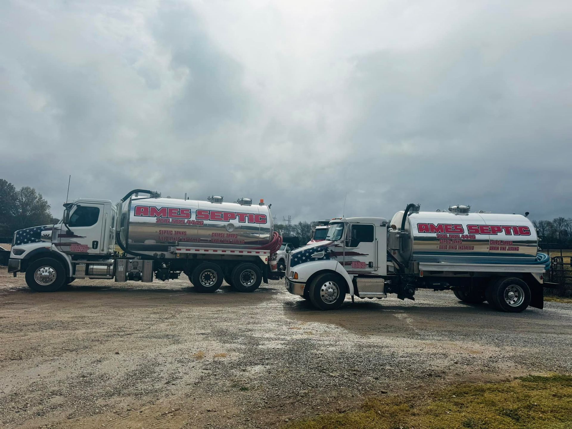 Two tanker trucks are parked next to each other in a gravel lot.