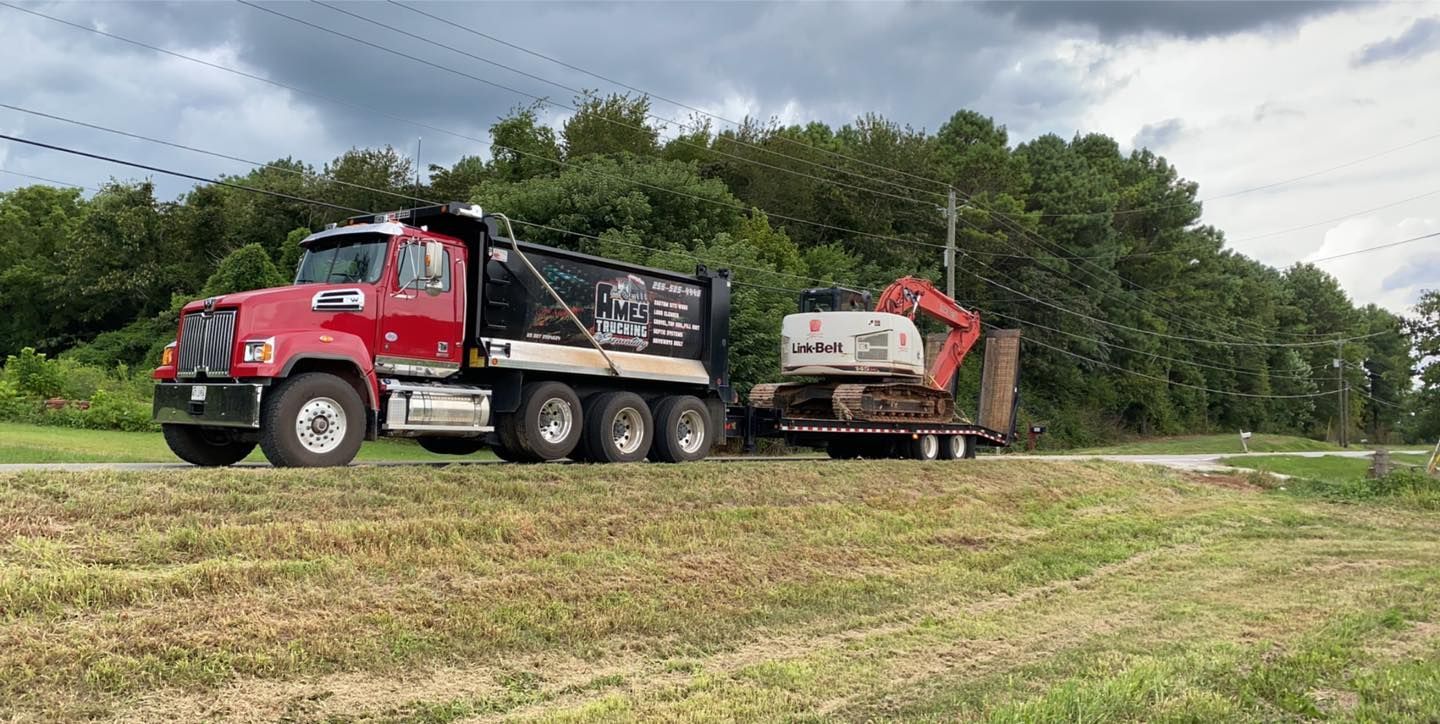 A red dump truck is driving down a road next to a field.