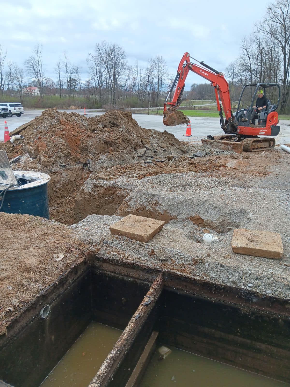 An excavator is digging a hole in the ground in a parking lot.