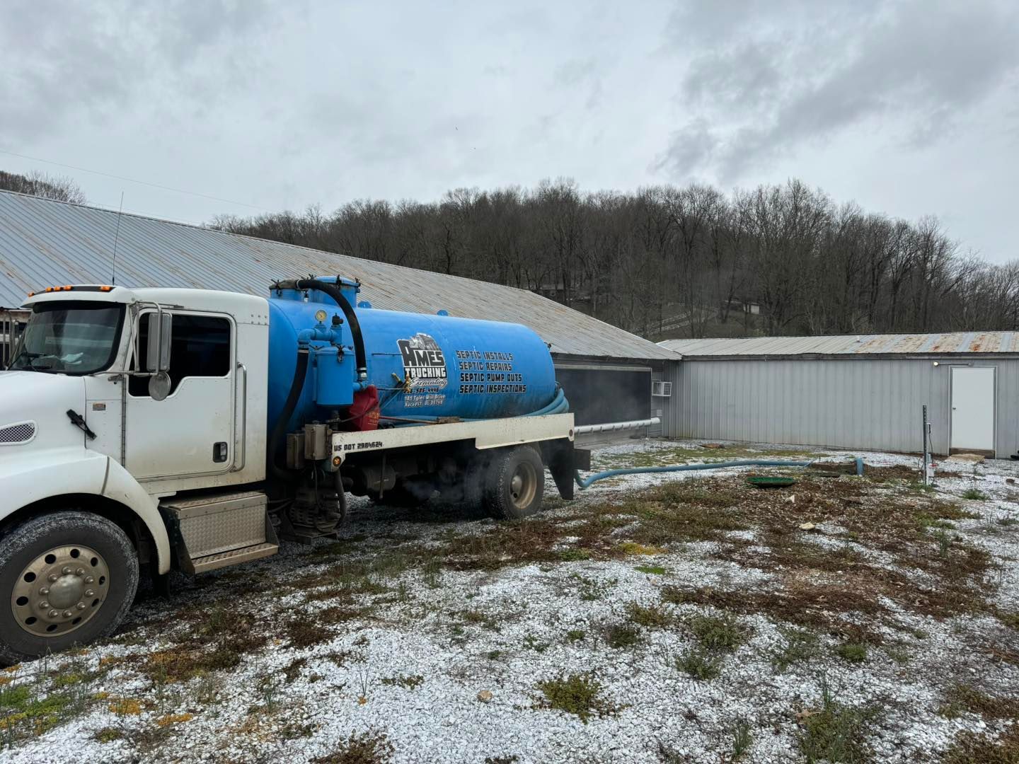 A blue vacuum truck is parked in a snowy field in front of a building.