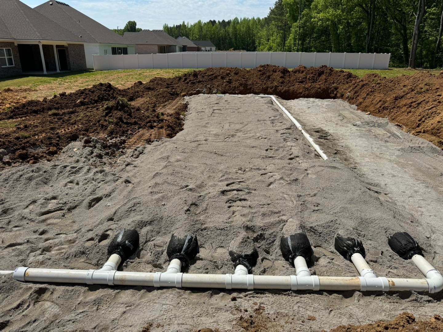 A row of pipes are sitting in the dirt in front of a house.