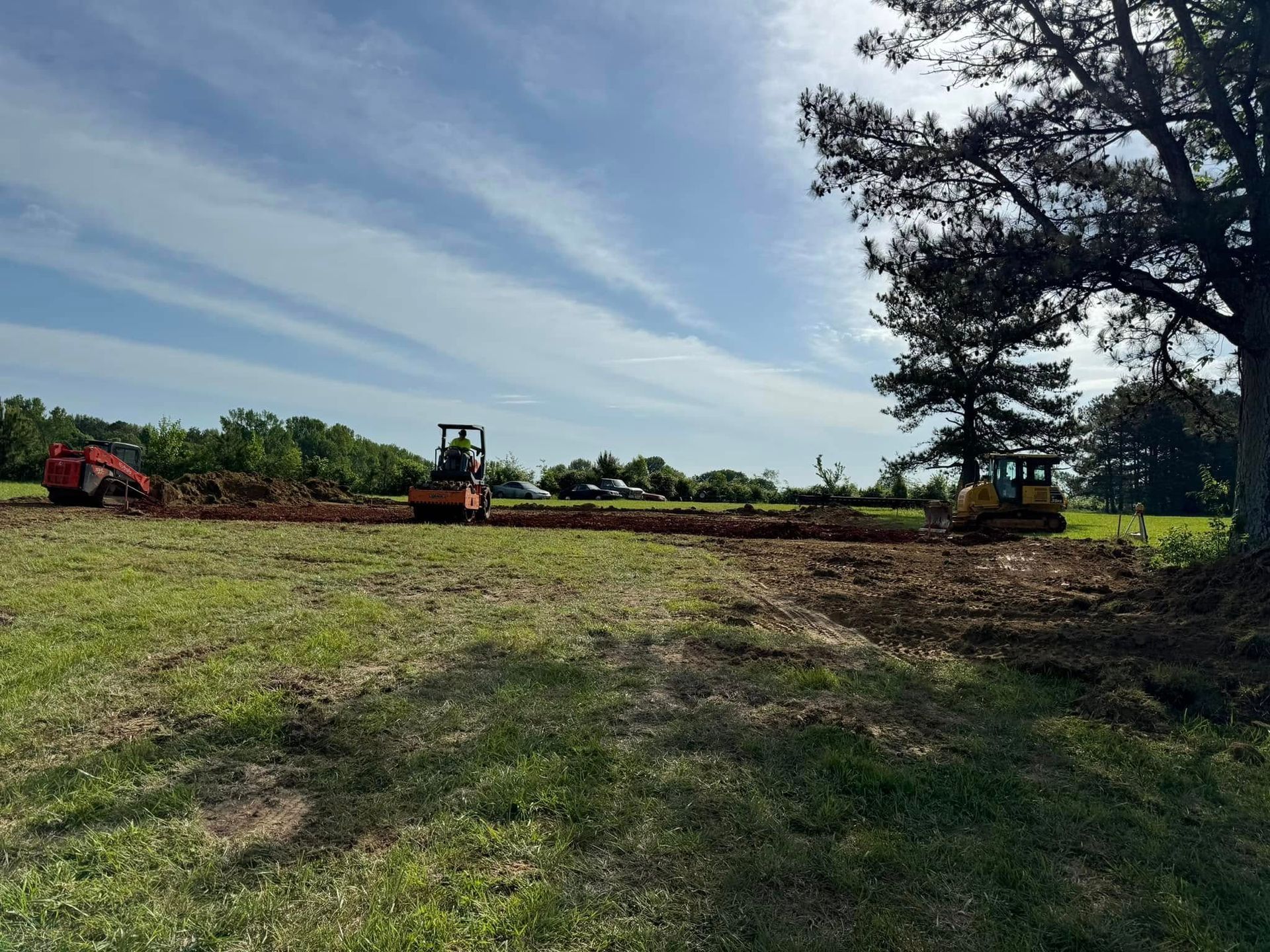 A group of construction vehicles are working in a grassy field.