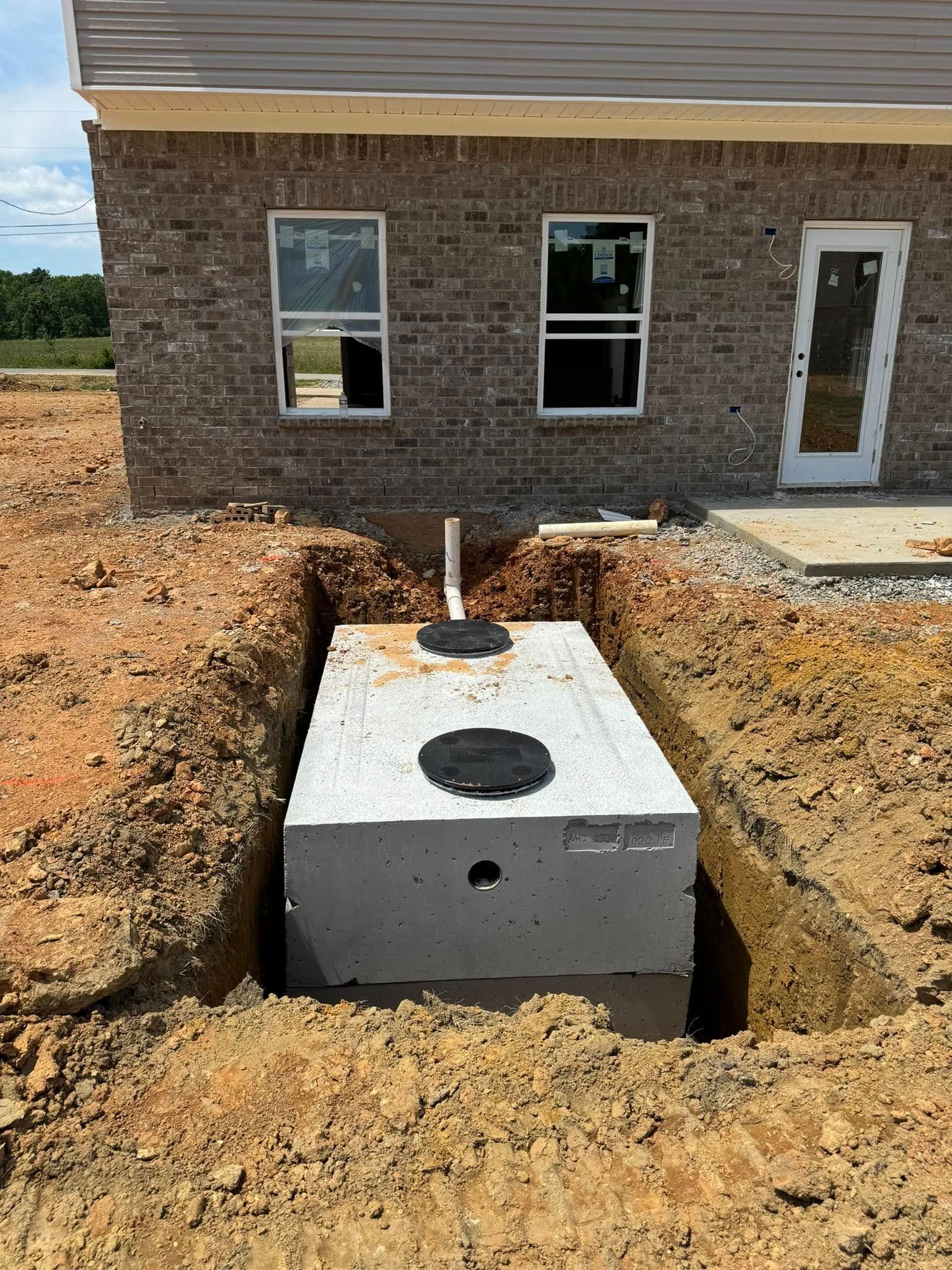A septic tank is being installed in the dirt in front of a house.