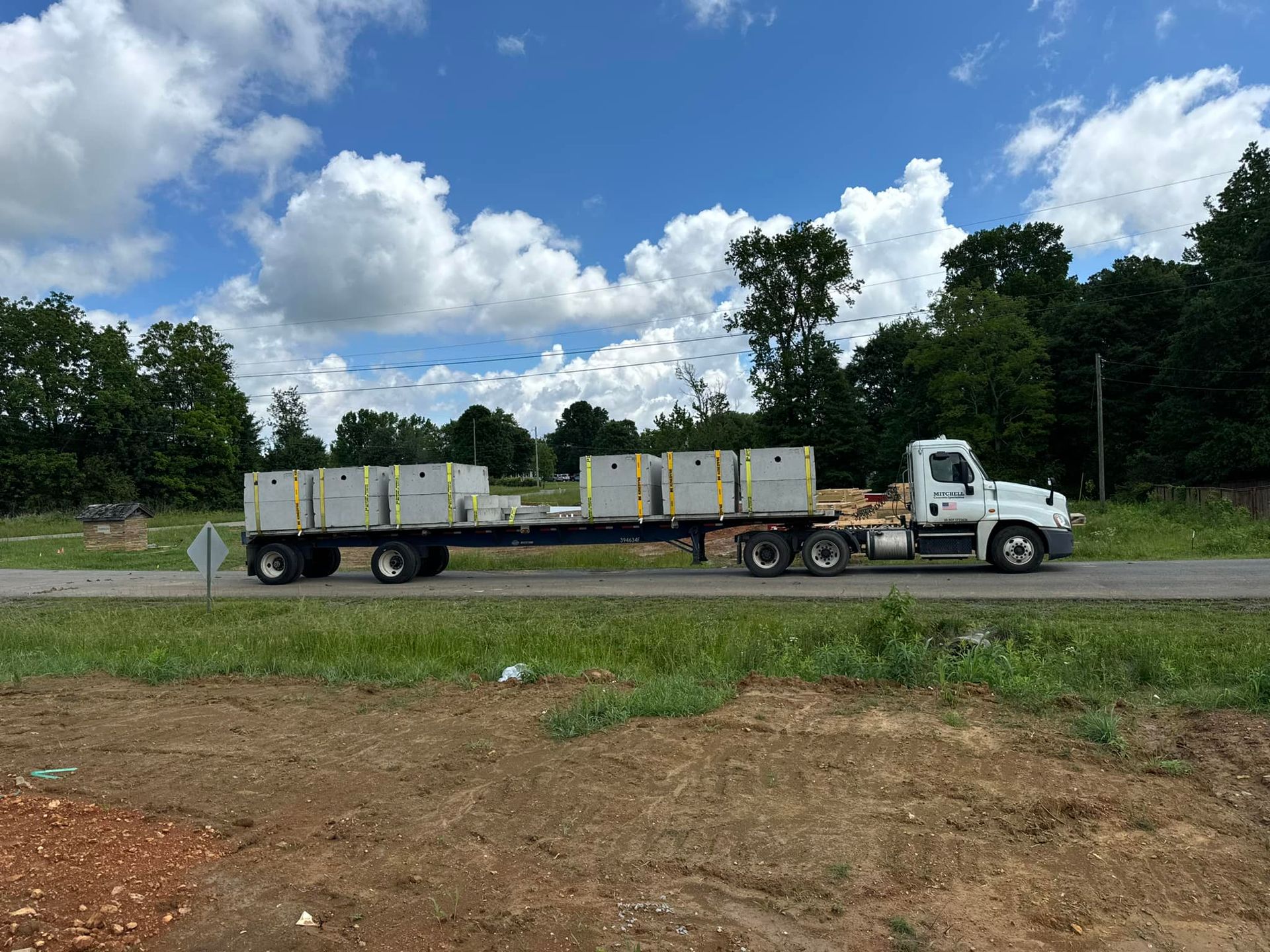 A white truck is driving down a road with a trailer full of concrete blocks.