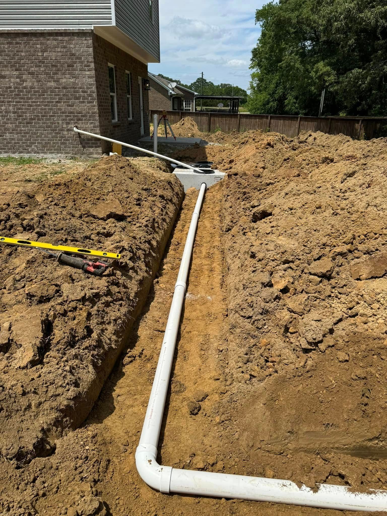 A drain pipe is being installed in the dirt in front of a house.