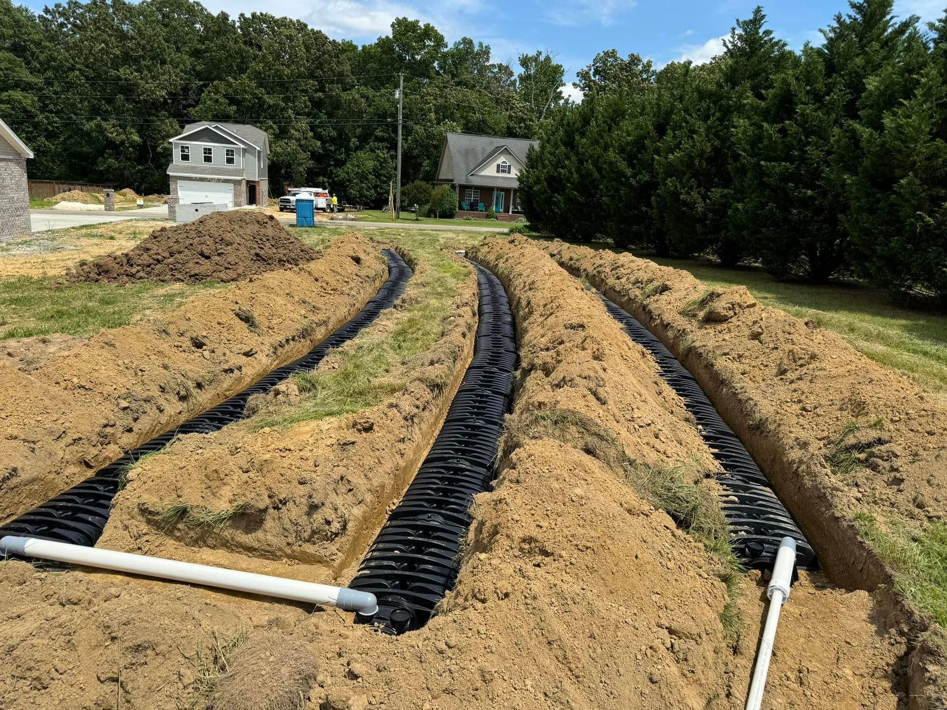 A drainage system is being installed in the dirt in front of a house.