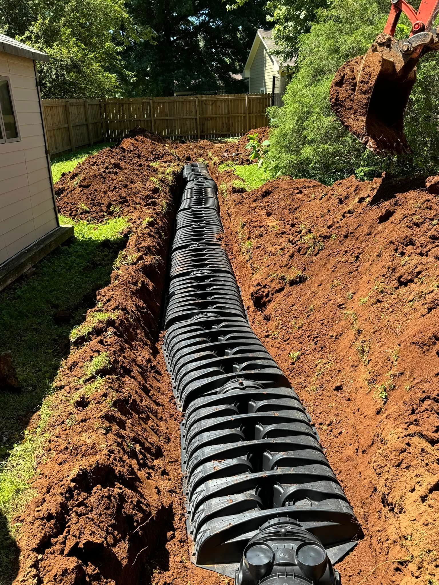 A large pipe is being installed in the dirt in a backyard.