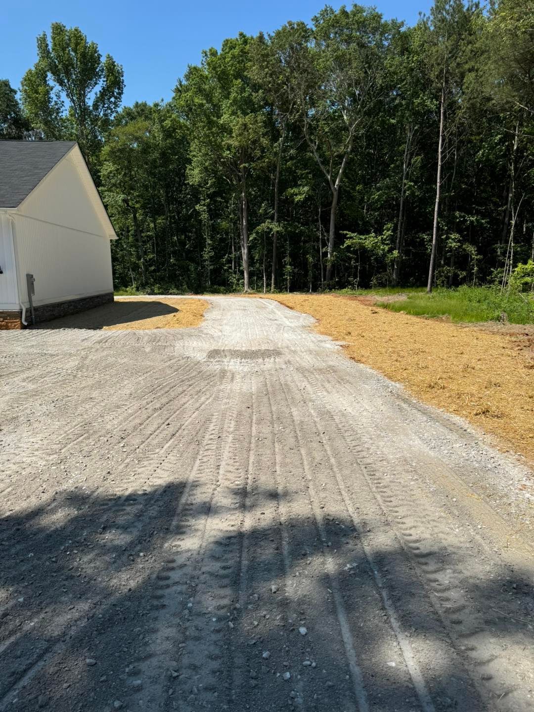 A dirt road leading to a white house in the woods.