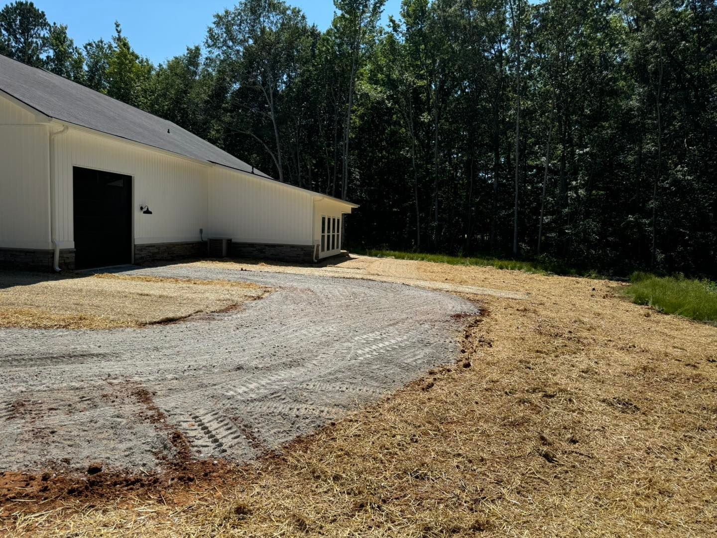 A white building with a black door is surrounded by trees