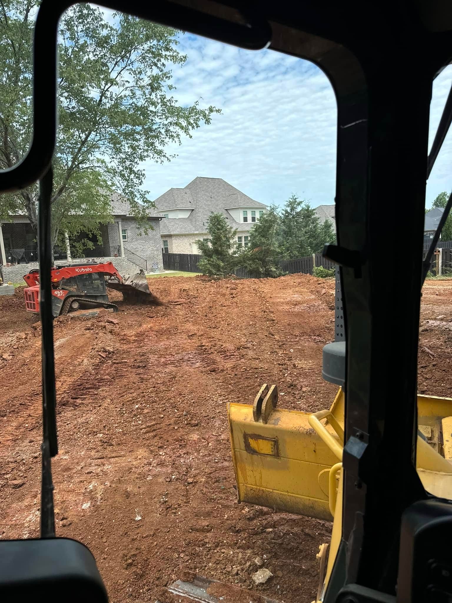 A bulldozer is moving dirt in a field in front of a house.