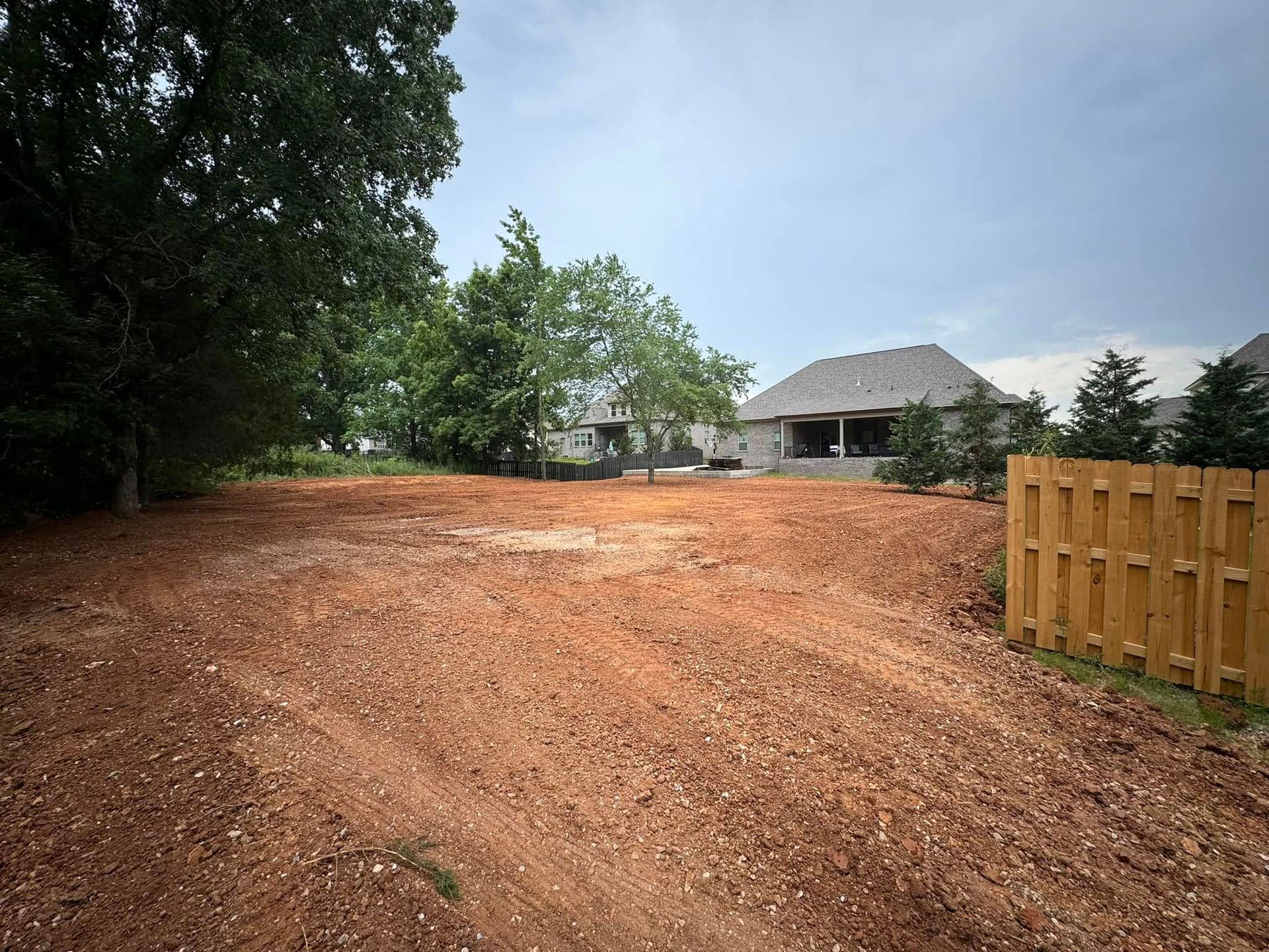 A dirt road with a wooden fence and a house in the background