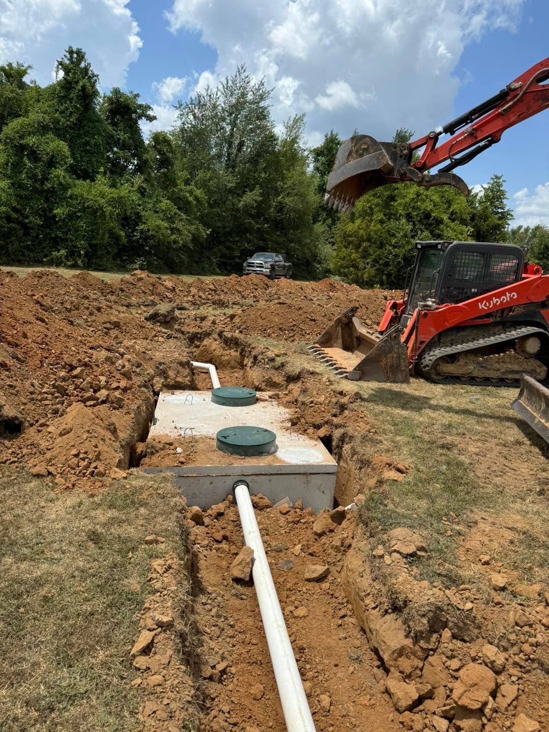 A bulldozer is digging a hole in the dirt next to a septic tank.