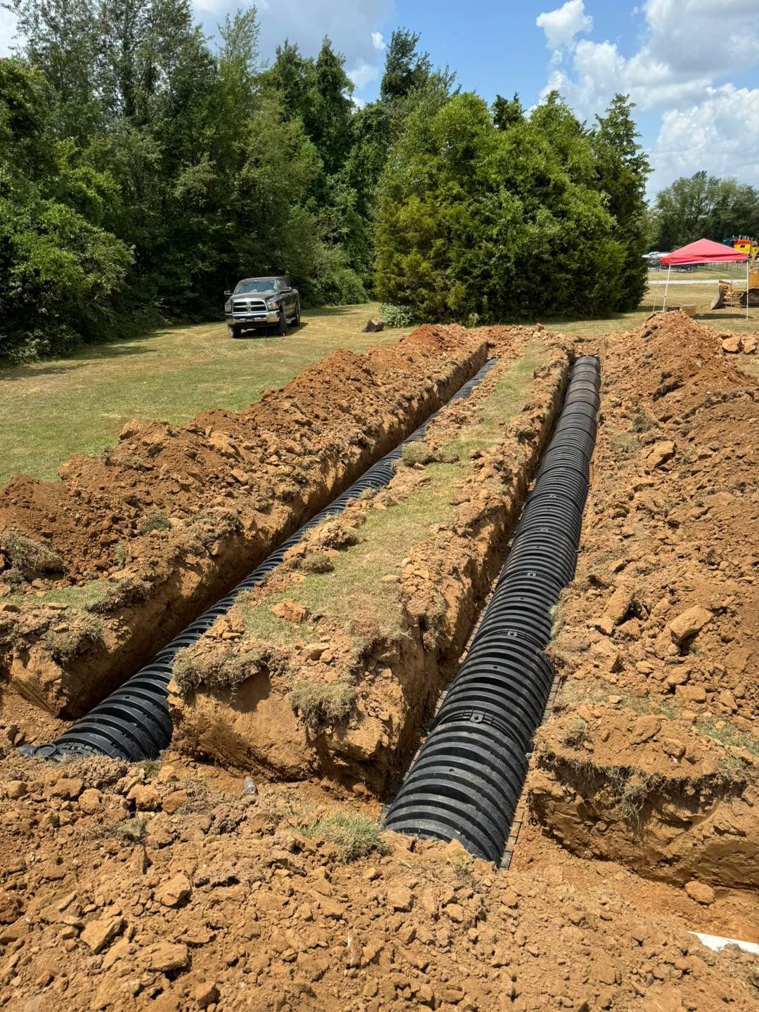 A row of drain pipes are being installed in a dirt field.