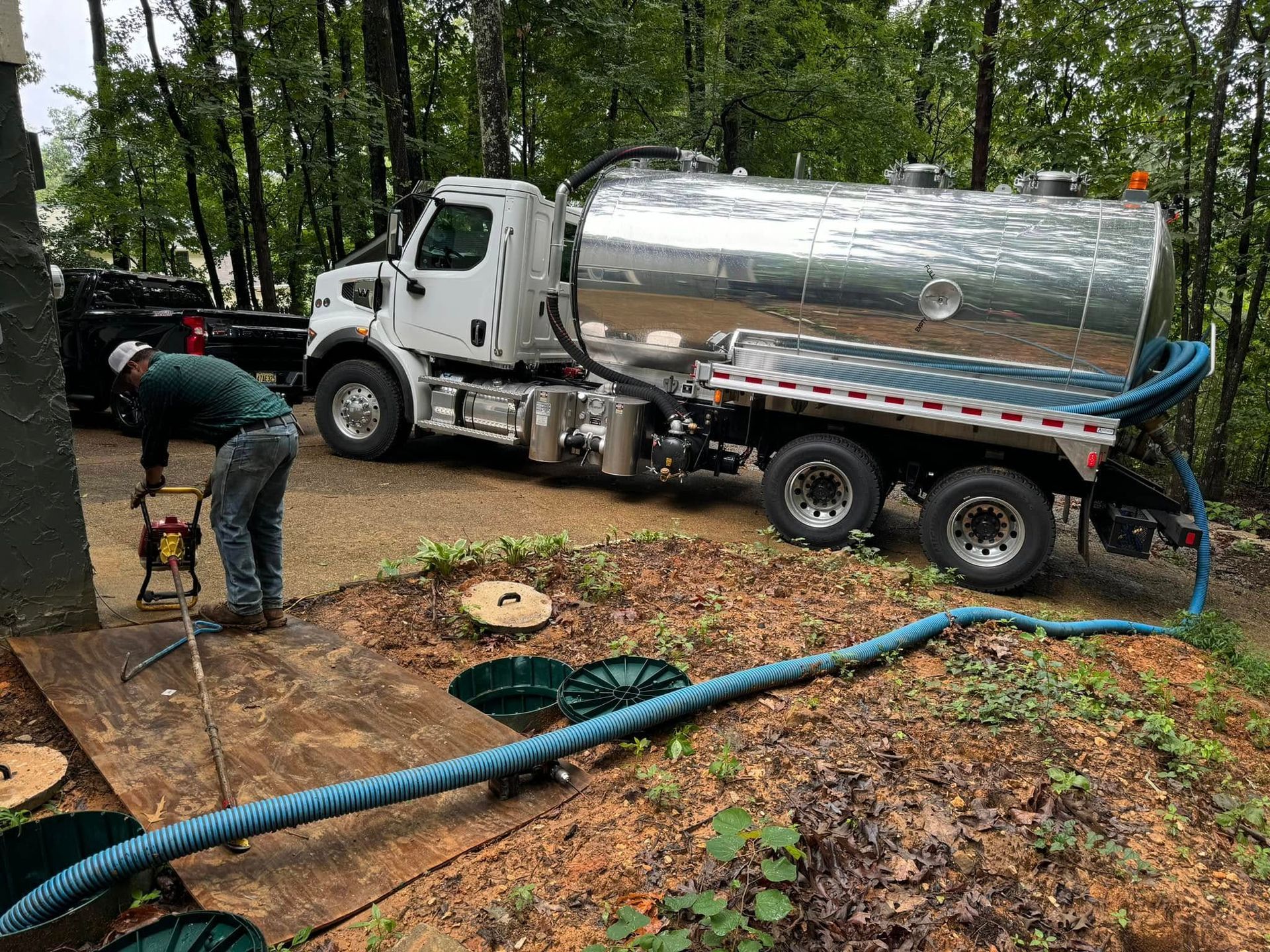 A man is working on a septic tank next to a vacuum truck.