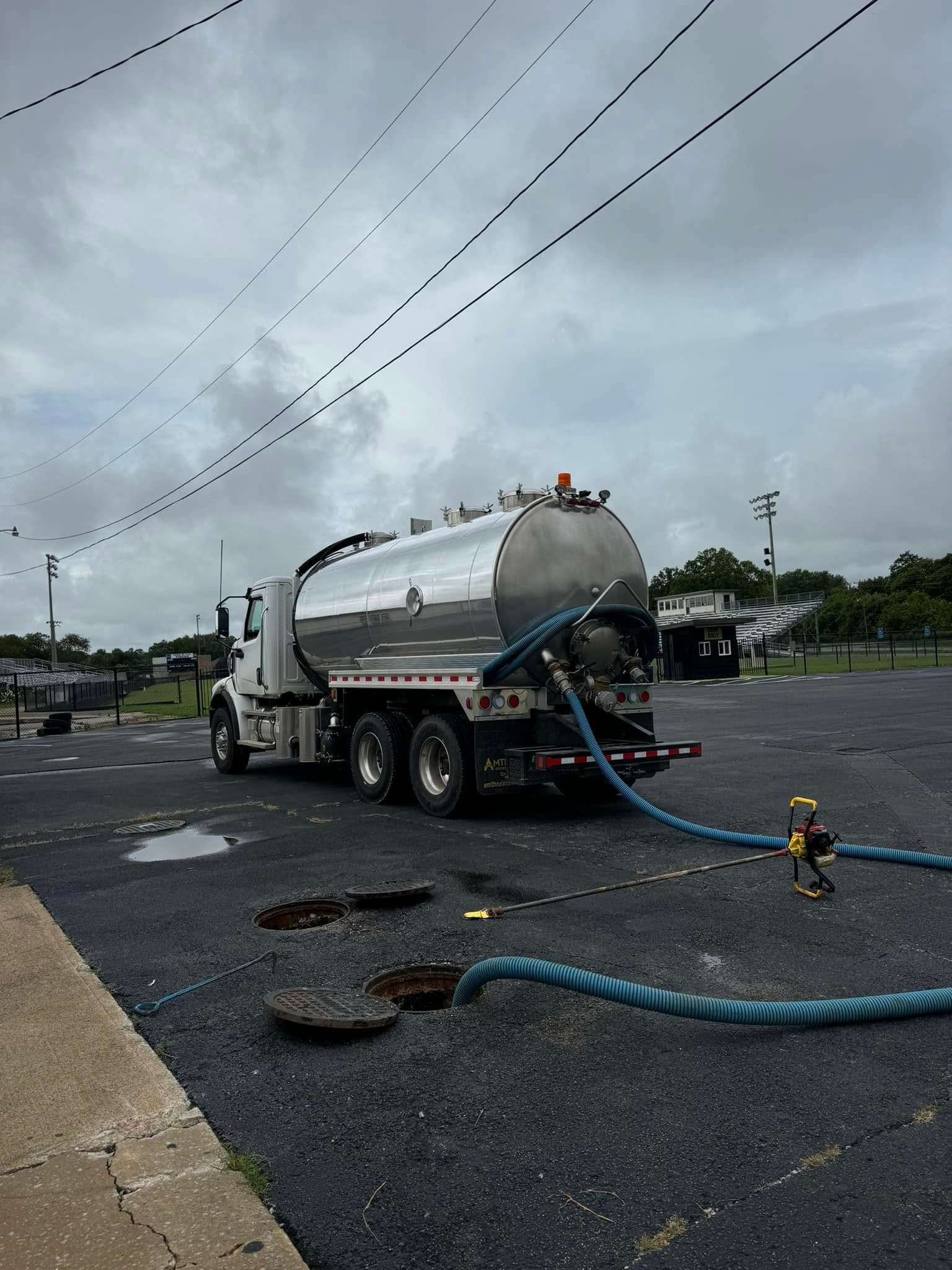 A vacuum truck is parked in a parking lot with a hose attached to it.