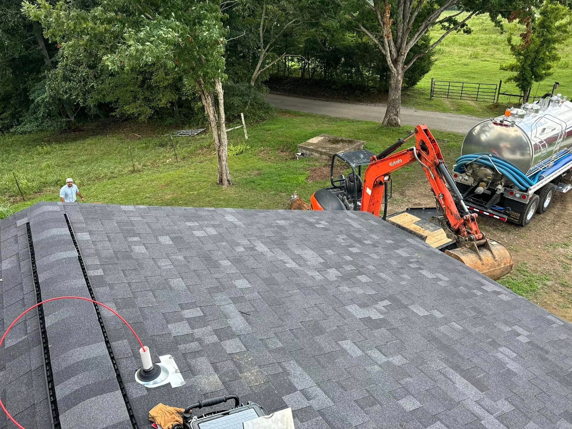 An excavator is sitting on top of a roof next to a tanker truck.