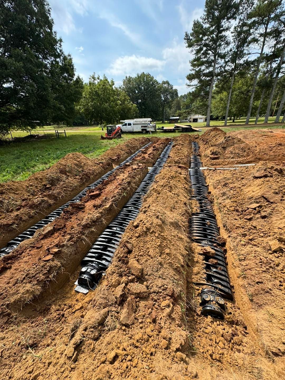A field of dirt with a tractor in the background and trees in the background.
