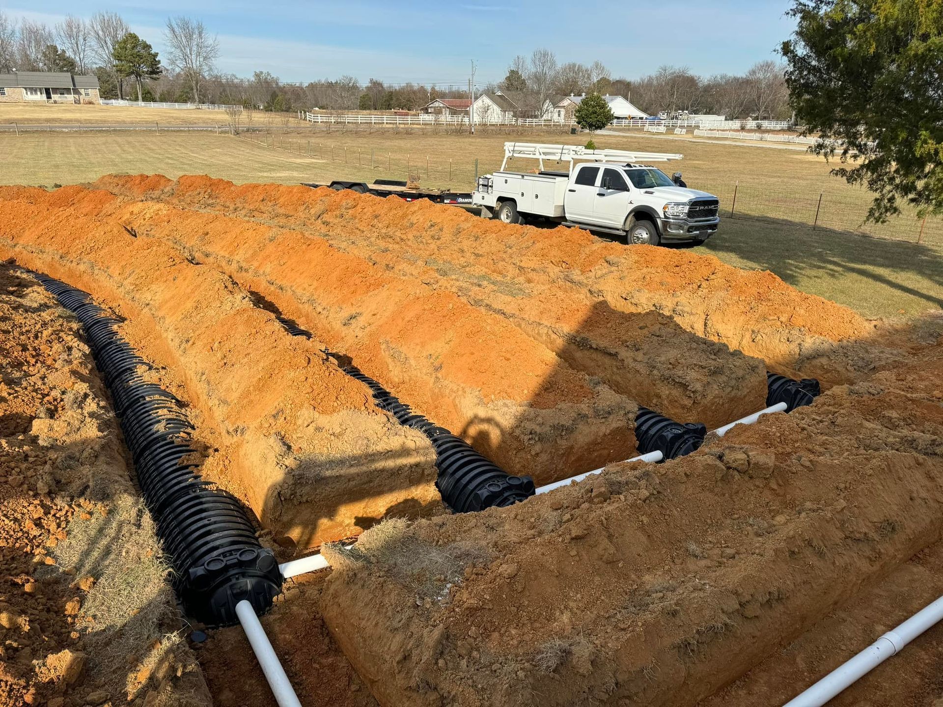 A row of white trucks are parked in a dirt field.