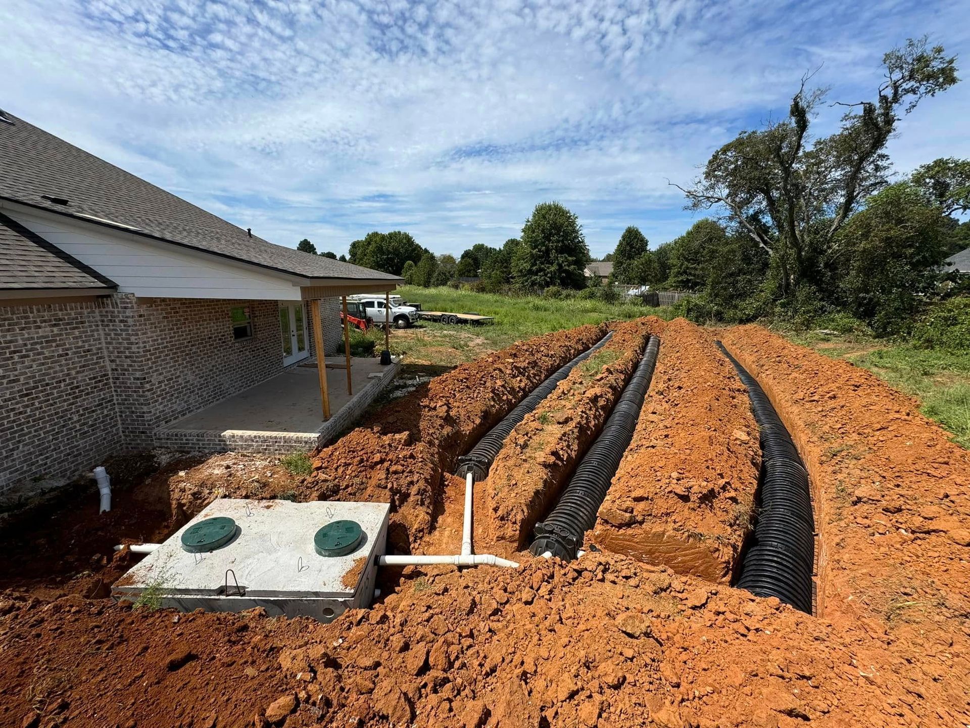 A septic tank is being installed in the dirt in front of a house.